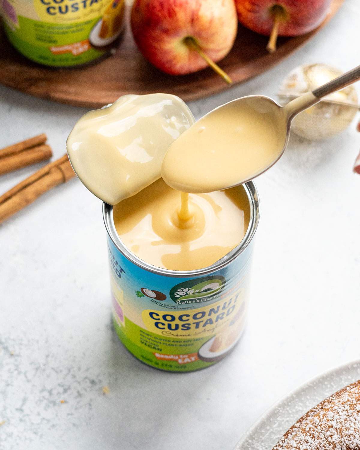 Spoon lifting creamy vegan coconut custard from an open can of Nature’s Charm coconut custard.