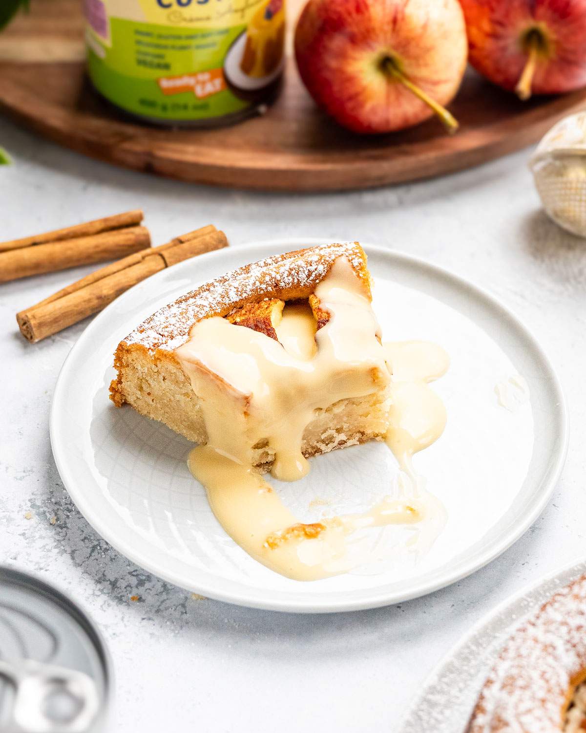 Slice of vegan apple cake served on a white plate with warm vegan custard poured over the top.