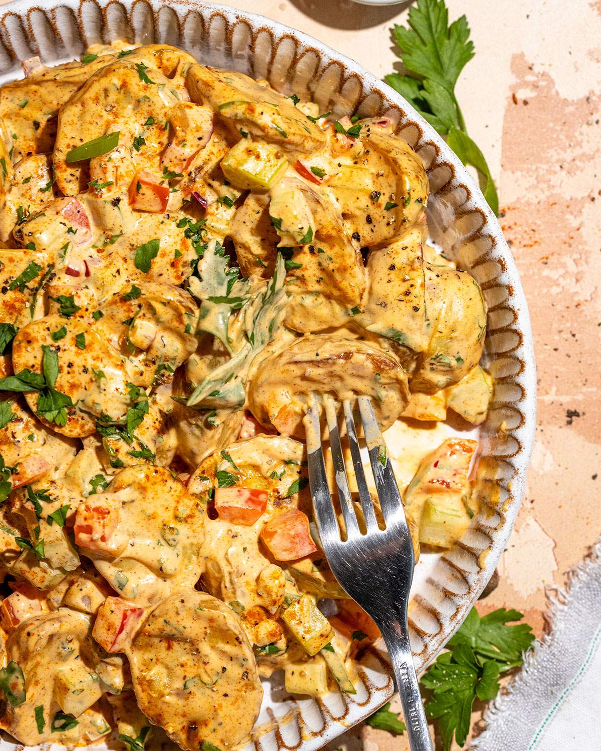 Creamy Cajun potato salad topped with sliced green onions and herbs and served with a fork.