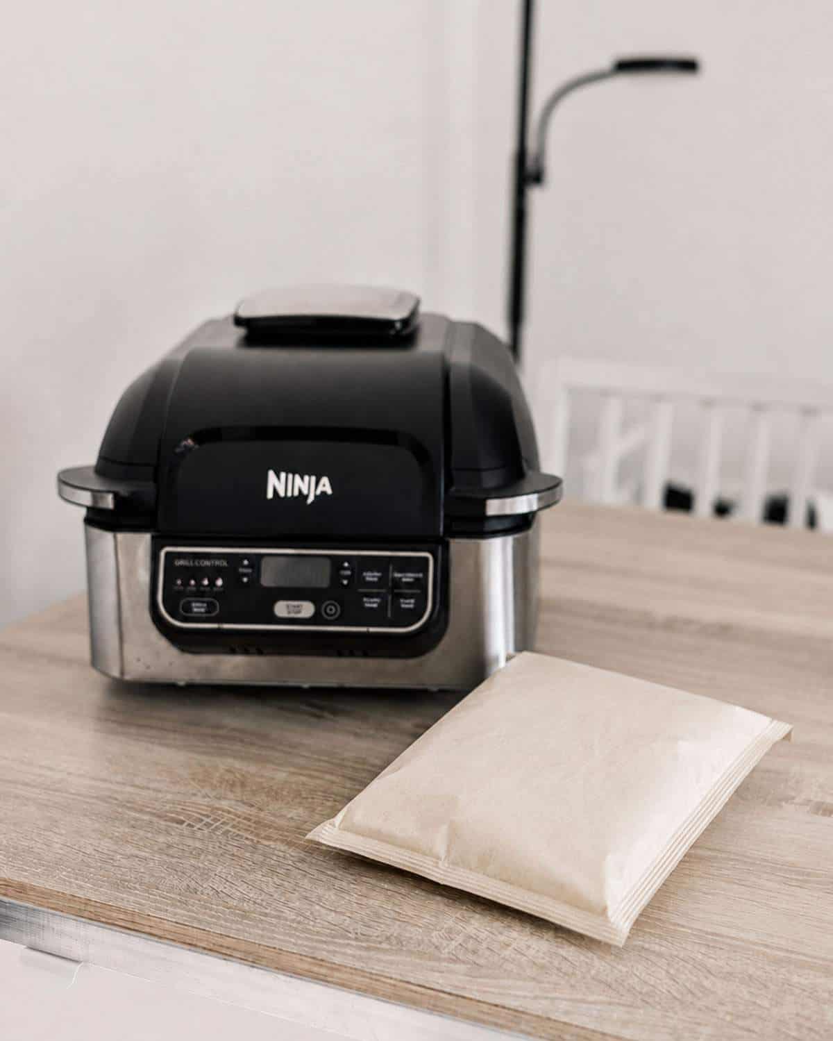 Unbranded bag of microwave popcorn on a kitchen counter beside a Ninja air fryer.