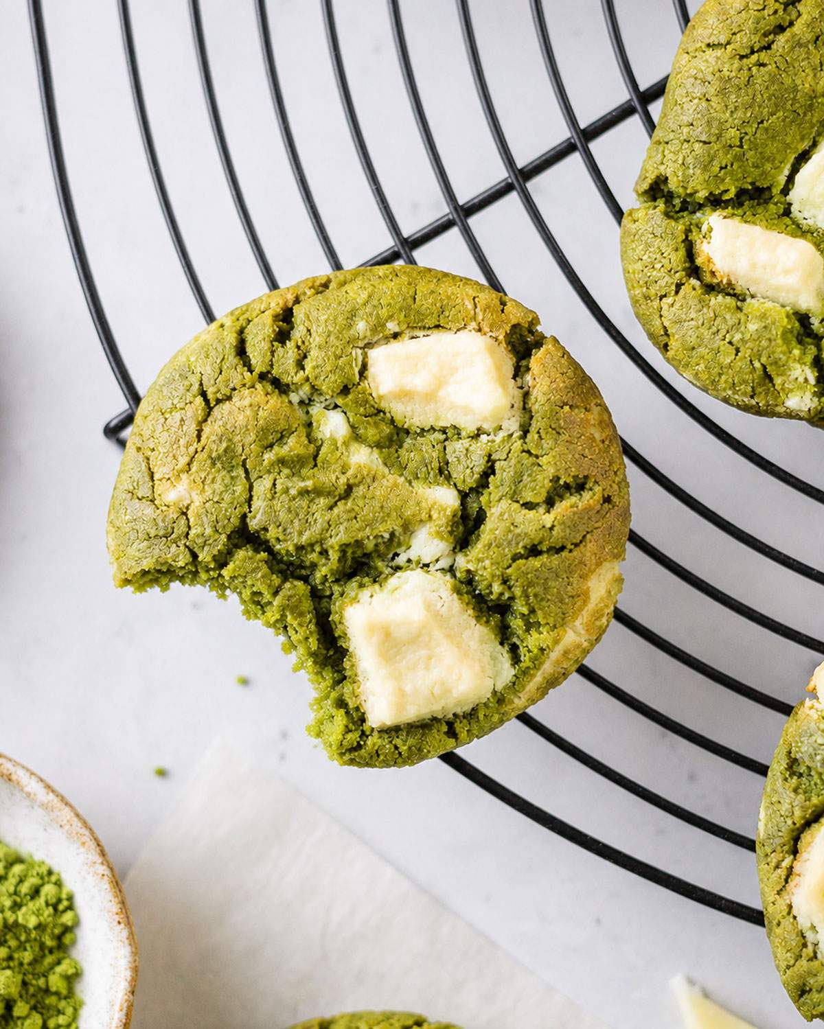 Close-up of a bitten matcha white chocolate cookie with a soft green centre and large creamy chocolate chunks.
