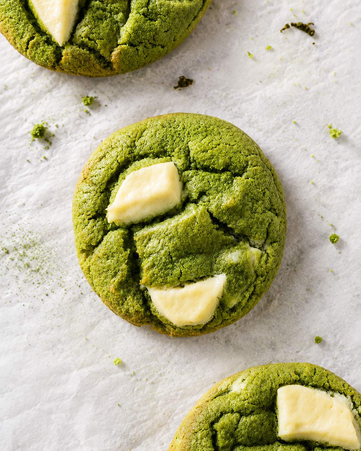 Close-up of a soft green matcha cookie with chunky pieces of melted white chocolate on crinkled baking parchment.