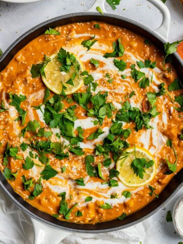 Easy vegan butter chickpea curry in a skillet with a creamy tomato sauce, coconut cream swirl, parsley, and lemon slices.
