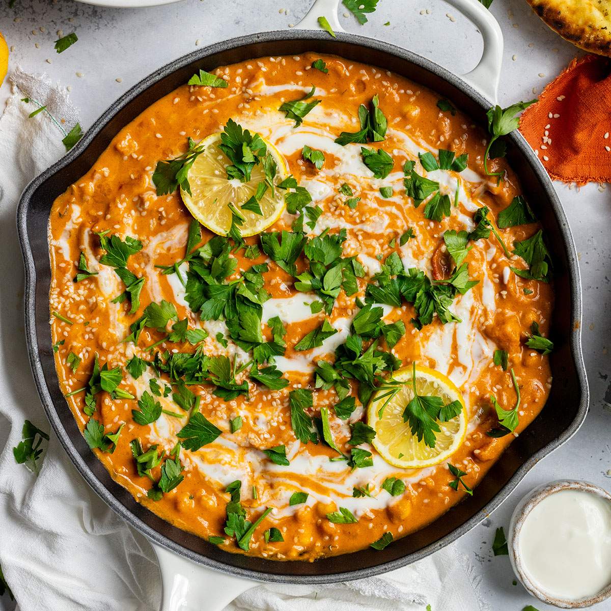 Easy vegan butter chickpea curry in a skillet with a creamy tomato sauce, coconut cream swirl, parsley, and lemon slices.
