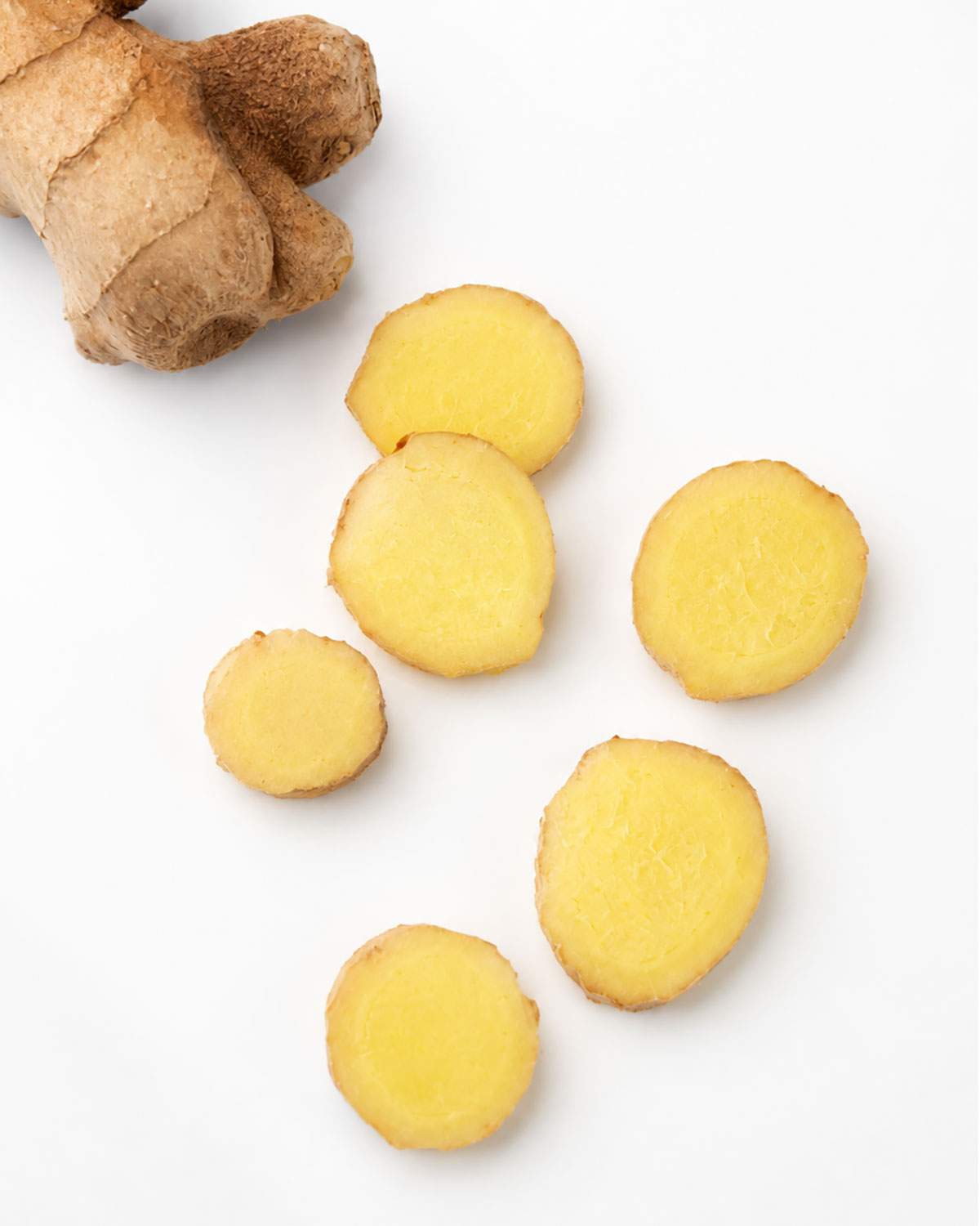 Fresh ginger root with several cut slices showing the pale yellow, firm interior of fresh ginger.