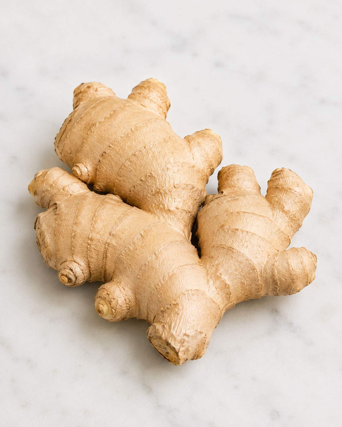 Whole fresh ginger root with firm, smooth golden-brown skin on a light marble surface.