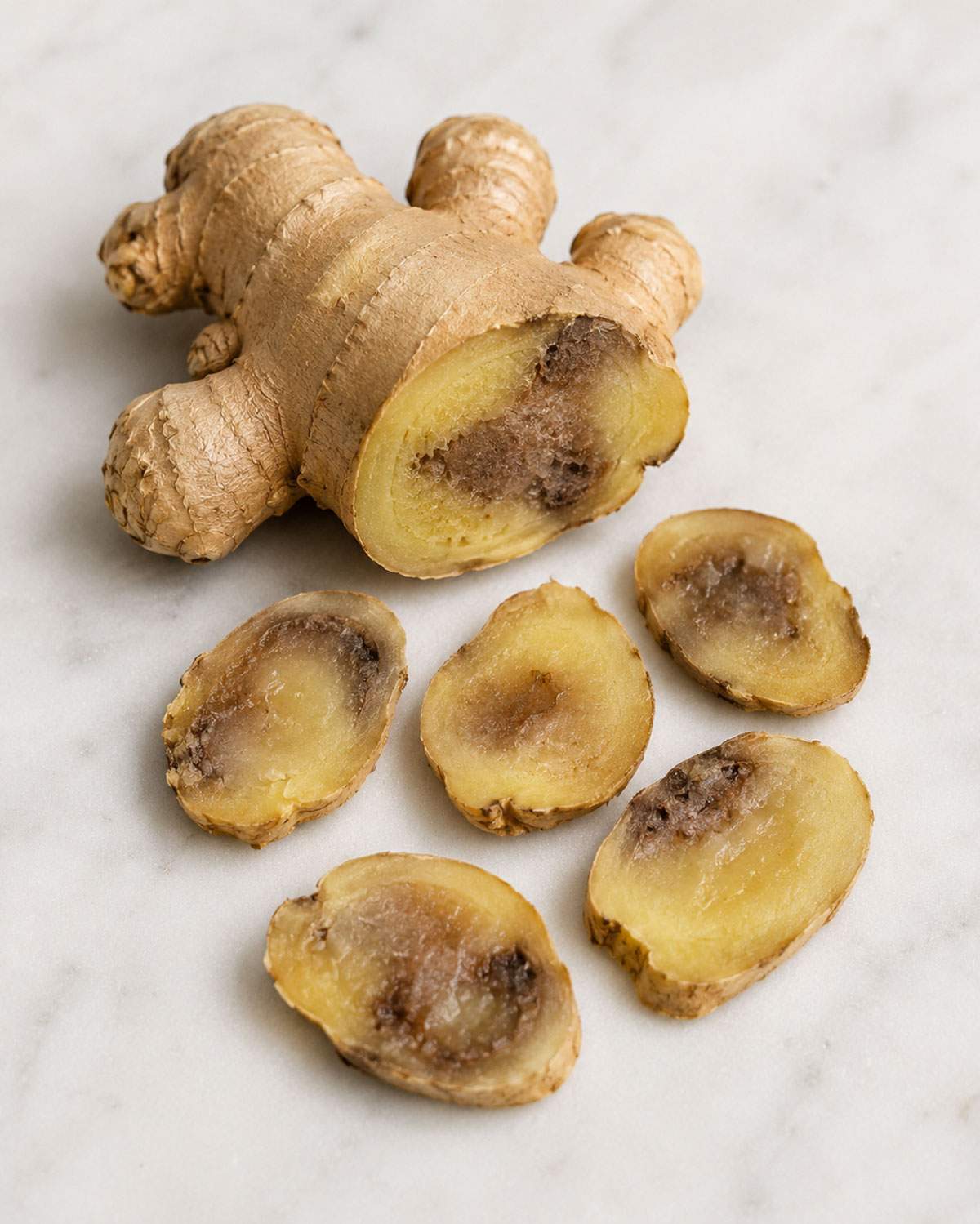 Ginger root with dark brown rotten patches on the cut ends and several discolored slices.