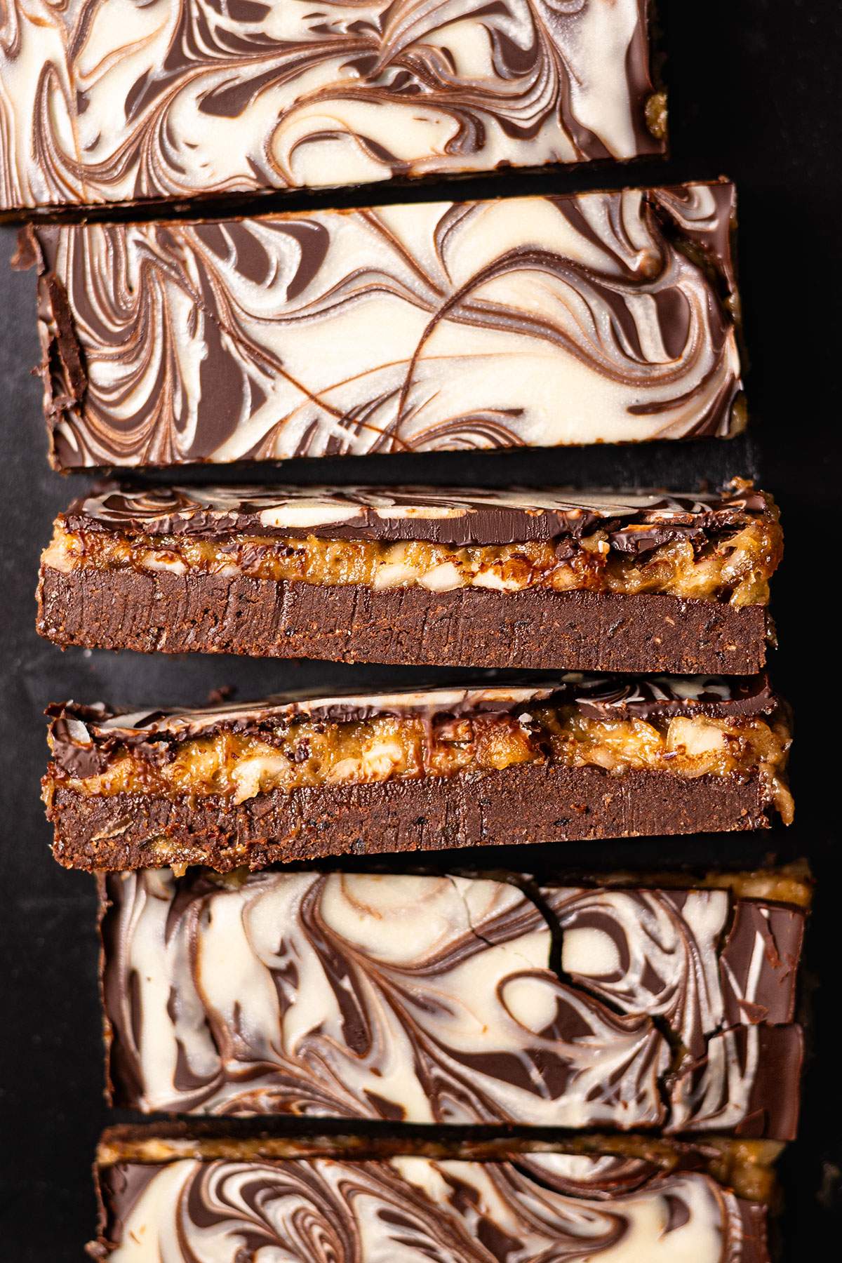 Close-up of date caramel protein bars with a fudgy chocolate base, golden caramel layer, and cream-colored swirls on top.