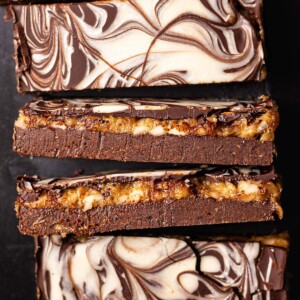 Close-up of date caramel protein bars with a fudgy chocolate base, golden caramel layer, and cream-colored swirls on top.