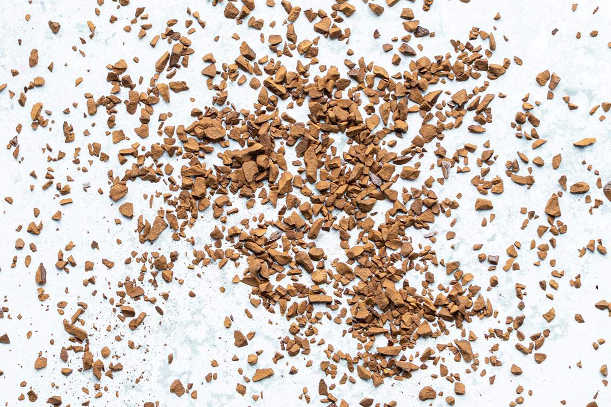 Instant coffee granules scattered across a pale stone surface.