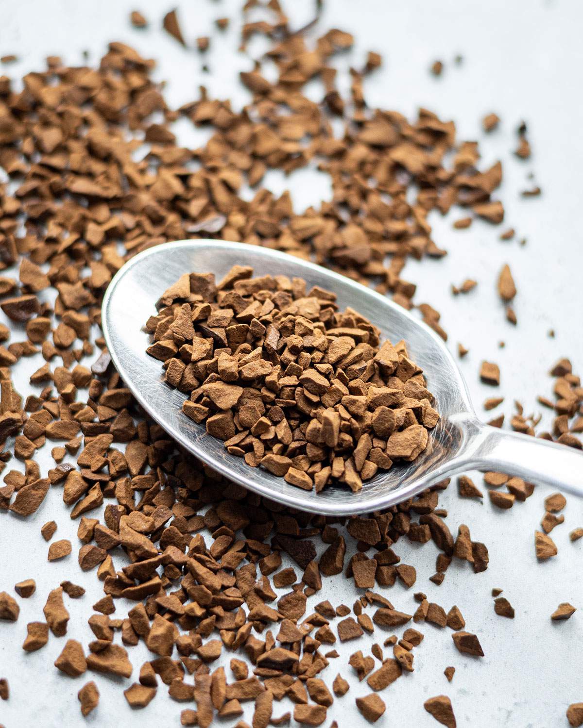 Close-up of a spoon filled with instant coffee granules surrounded by loose coffee crystals.
