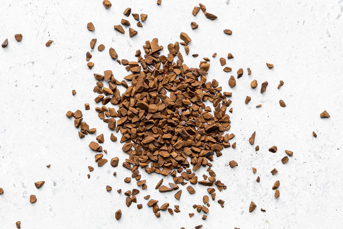 Small pile of dry instant coffee granules on a light stone background.